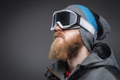 Retrato do close-up de um homem com uma barba vermelha que veste um chapéu do inverno, um revestimento e uns vidros protetores da fotografia de stock royalty free Retrato do close-up de um homem com uma barba vermelha que veste um chapéu do inverno, um revestimento e uns vidros protetores da fotografia de stock royalty free