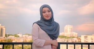 Retrato do estudante muçulmano no hijab que sorri na posição da câmera no balcão com grande opinião da cidade filme Retrato do estudante muçulmano no hijab que sorri na posição da câmera no balcão com grande opinião da cidade filme