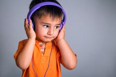 Retrato do estúdio de um menino engraçado pequeno com os olhos marrons nos fones de ouvido que escuta a música em um fundo cinzen Fotografia de Stock Royalty Free Retrato do estúdio de um menino engraçado pequeno com os olhos marrons nos fones de ouvido que escuta a música em um fundo cinzen Fotografia de Stock Royalty Free