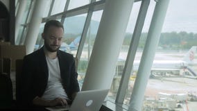 Retrato do homem de negócios novo que está datilografando um email em seu portátil no aeroporto video estoque Retrato do homem de negócios novo que está datilografando um email em seu portátil no aeroporto video estoque
