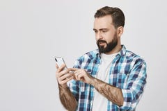 Retrato do indivíduo atrativo com a barba e o bigode que guardam o smartphone e da rede da consultação com surpreendido e deixado foto de stock royalty free Retrato do indivíduo atrativo com a barba e o bigode que guardam o smartphone e da rede da consultação com surpreendido e deixado foto de stock royalty free