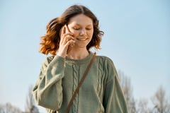 Retrato exterior da menina adolescente de sorriso que anda e que fala no telefone, fundo do céu azul fotografia de stock royalty free Retrato exterior da menina adolescente de sorriso que anda e que fala no telefone, fundo do céu azul fotografia de stock royalty free