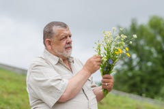 Retrato exterior do homem superior com o ramalhete de flores selvagens para sua esposa imagens de stock royalty free Retrato exterior do homem superior com o ramalhete de flores selvagens para sua esposa imagens de stock royalty free