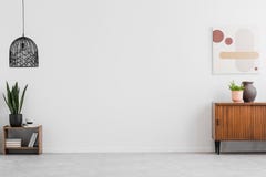 Retro, wooden cabinet and a painting in an empty living room interior with white walls and copy space place for a sofa. Real photo