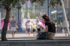 RIGA, LATVIA - JULY 18, 2018: A Young Woman Sits On The Bench At The Edge Of The Street And Looks At The Phone. Royalty Free Stock Photos