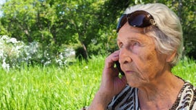 Rijpe vrouw met een telefoon Een teruggetrokken vrouw spreekt op haar mobiele telefoon in het park Oude vrouw in zonnebril met stock videobeelden Rijpe vrouw met een telefoon Een teruggetrokken vrouw spreekt op haar mobiele telefoon in het park Oude vrouw in zonnebril met stock videobeelden