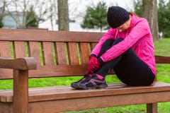 Riposo stanco o depresso dell'atleta femminile su un banco un giorno di inverno freddo sulla pista di addestramento di un parco u immagine stock libera da diritti Riposo stanco o depresso dell'atleta femminile su un banco un giorno di inverno freddo sulla pista di addestramento di un parco u immagine stock libera da diritti