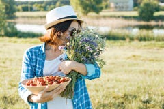 Ritratto all'aperto di estate della donna adulta con le fragole, mazzo dei wildflowers, cappello di paglia ed occhiali da sole Fo fotografia stock libera da diritti Ritratto all'aperto di estate della donna adulta con le fragole, mazzo dei wildflowers, cappello di paglia ed occhiali da sole Fo fotografia stock libera da diritti