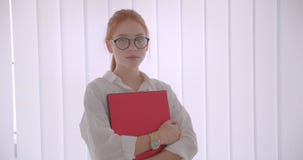 Ritratto del primo piano di giovane donna di affari caucasica graziosa della testarossa in vetri che tengono il computer portatil video d archivio Ritratto del primo piano di giovane donna di affari caucasica graziosa della testarossa in vetri che tengono il computer portatil video d archivio