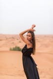 Ritratto di bella giovane donna in vestito nero che posa sulla sabbia nel deserto immagine stock Ritratto di bella giovane donna in vestito nero che posa sulla sabbia nel deserto immagine stock