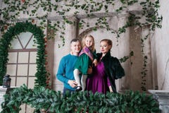 Ritratto di giovane famiglia amichevole che esamina macchina fotografica sulla mattina di natale Padre, madre e figlia fotografia stock libera da diritti Ritratto di giovane famiglia amichevole che esamina macchina fotografica sulla mattina di natale Padre, madre e figlia fotografia stock libera da diritti