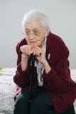 Ritratto di una donna senior che si siede sul letto con il bastone da passeggio a casa fotografia stock libera da diritti Ritratto di una donna senior che si siede sul letto con il bastone da passeggio a casa fotografia stock libera da diritti