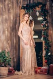 Ritratto integrale di una donna bionda elegante sexy in un vestito dorato lungo vicino allo specchio decorato con i rami di Natal fotografie stock libere da diritti Ritratto integrale di una donna bionda elegante sexy in un vestito dorato lungo vicino allo specchio decorato con i rami di Natal fotografie stock libere da diritti