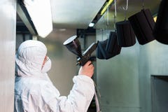 Rivestimento della polvere delle parti di metallo Un uomo in un vestito protettivo spruzza la pittura della polvere da una pistol immagine stock Rivestimento della polvere delle parti di metallo Un uomo in un vestito protettivo spruzza la pittura della polvere da una pistol immagine stock