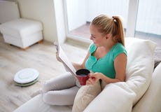 Rivista felice della lettura della donna con la tazza di tè a casa fotografia stock Rivista felice della lettura della donna con la tazza di tè a casa fotografia stock