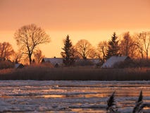 Rivière Atmata, maisons et arbres neigeux dans des couleurs de coucher du soleil, Lithuanie photo stock Rivière Atmata, maisons et arbres neigeux dans des couleurs de coucher du soleil, Lithuanie photo stock