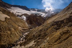 Rivière traversant le canyon avec des fumerolles à l'intérieur de cratère de volcan de Mutnovsky photos stock Rivière traversant le canyon avec des fumerolles à l'intérieur de cratère de volcan de Mutnovsky photos stock