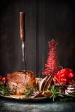 Roasted a découpé le jambon de Noël avec la fourchette et la décoration en tranches de fête rouge de vacances au fond en bois fon photographie stock libre de droits Roasted a découpé le jambon de Noël avec la fourchette et la décoration en tranches de fête rouge de vacances au fond en bois fon photographie stock libre de droits