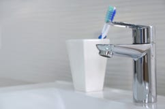 Robinet argenté brillant en gros plan et brosses à dents dans un verre blanc photos stock Robinet argenté brillant en gros plan et brosses à dents dans un verre blanc photos stock
