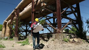 Robociarz w żółtym ciężkim kapeluszu z projektów rysunkami przy upał elektrownią zbiory wideo Robociarz w żółtym ciężkim kapeluszu z projektów rysunkami przy upał elektrownią zbiory wideo