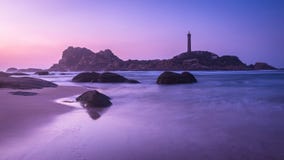 Roches sur la plage, les vagues, l'île et le phare au lever de soleil images libres de droits Roches sur la plage, les vagues, l'île et le phare au lever de soleil images libres de droits