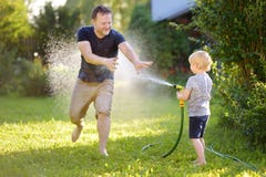 Rolig pys med hans fader som spelar med tr?dg?rdslangen i solig tr?dg?rd F?rskolebarnbarn som har gyckel med sprej av vatten arkivbilder Rolig pys med hans fader som spelar med tr?dg?rdslangen i solig tr?dg?rd F?rskolebarnbarn som har gyckel med sprej av vatten arkivbilder
