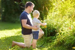 Rolig pys med hans fader som spelar med tr?dg?rdslangen i solig tr?dg?rd F?rskolebarnbarn som har gyckel med sprej av vatten royaltyfri fotografi Rolig pys med hans fader som spelar med tr?dg?rdslangen i solig tr?dg?rd F?rskolebarnbarn som har gyckel med sprej av vatten royaltyfri fotografi