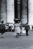 ROMA, ITÁLIA, 1970 - uma família dos emigrantes anda perto da colunata de S Peter Square com uma caixa de cartão e uma mala de vi fotografia de stock ROMA, ITÁLIA, 1970 - uma família dos emigrantes anda perto da colunata de S Peter Square com uma caixa de cartão e uma mala de vi fotografia de stock