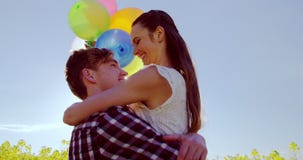 Romantische Paare, die bunte Ballone halten und auf dem Senfgebiet sich umfassen stock footage Romantische Paare, die bunte Ballone halten und auf dem Senfgebiet sich umfassen stock footage