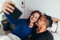 Romantiska blandras- par som tar selfie på säng arkivbild Romantiska blandras- par som tar selfie på säng arkivbild