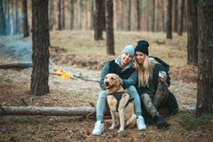 Romantiska par med hunden som sitter nära brasan, höstskogbakgrund Ung blond kvinna och stilig man royaltyfri foto Romantiska par med hunden som sitter nära brasan, höstskogbakgrund Ung blond kvinna och stilig man royaltyfri foto