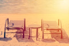 Romantiskt feriesemesterbegrepp Par av soldagdrivare och en tabell på en öde strand med solen under solnedgång royaltyfri foto Romantiskt feriesemesterbegrepp Par av soldagdrivare och en tabell på en öde strand med solen under solnedgång royaltyfri foto