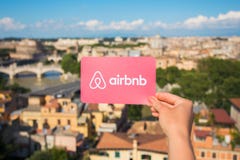 Rome, Italy - May 13, 2018: Person holding Airbnb logo in hand with city in background. royalty free stock images Rome, Italy - May 13, 2018: Person holding Airbnb logo in hand with city in background. royalty free stock images