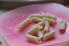 Rosa plast- platta och Penne pasta Behandla som ett barn lite äter pennepastagluten fritt royaltyfri bild Rosa plast- platta och Penne pasta Behandla som ett barn lite äter pennepastagluten fritt royaltyfri bild