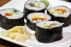 Rotoli di sushi su un piatto bianco con la salsa di soia Contro il contesto di una tavola di legno d'annata immagine stock Rotoli di sushi su un piatto bianco con la salsa di soia Contro il contesto di una tavola di legno d'annata immagine stock