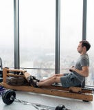 Rudern mit Energie Seitenansicht des jungen Mannes in der Sportkleidung, die Rudersport vor Fenster an der Turnhalle tut lizenzfreies stockfoto Rudern mit Energie Seitenansicht des jungen Mannes in der Sportkleidung, die Rudersport vor Fenster an der Turnhalle tut lizenzfreies stockfoto