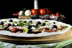 Rå okokt pizza med peperonisalami, svarta oliv, basilika och ost arkivbild Rå okokt pizza med peperonisalami, svarta oliv, basilika och ost arkivbild
