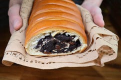 Rötliches frisches Brötchen mit Mohnlügen in den Händen des Mannes auf hellem Spitzegewebe lizenzfreies stockbild Rötliches frisches Brötchen mit Mohnlügen in den Händen des Mannes auf hellem Spitzegewebe lizenzfreies stockbild