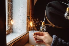 Ręki dziewczyna trzyma Bengalia światła na tle okno, kapelusz i dekoruje z dowodzonymi światłami zdjęcie stock Ręki dziewczyna trzyma Bengalia światła na tle okno, kapelusz i dekoruje z dowodzonymi światłami zdjęcie stock