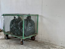 Sacs de déchets noirs disposés dans un chariot vert sur le plancher de ciment près du mur blanc, chariot de déchets pour la réuti image libre de droits Sacs de déchets noirs disposés dans un chariot vert sur le plancher de ciment près du mur blanc, chariot de déchets pour la réuti image libre de droits