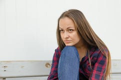 Sad beautiful girl with long hair and a red and blue checkered shirt and jeans sitting on bench. close view royalty free stock photography Sad beautiful girl with long hair and a red and blue checkered shirt and jeans sitting on bench. close view royalty free stock photography