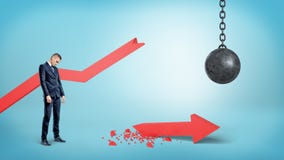 A sad businessman stands near a broken red statistic arrow with a wrecking ball hanging nearby. Stock Photography A sad businessman stands near a broken red statistic arrow with a wrecking ball hanging nearby. Stock Photography