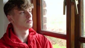 Sad depressed teen male teenager young man adult sitting looking out of a window stock video footage Sad depressed teen male teenager young man adult sitting looking out of a window stock video footage