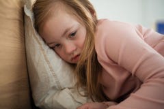Sad little girl with Down syndrome lying on bed at home.