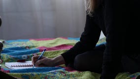 Sad young female student writes in her journal while sitting on a bed. adolescent experiences. slow motion stock video Sad young female student writes in her journal while sitting on a bed. adolescent experiences. slow motion stock video