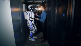 Sala do servidor com um robô que está sendo ajustado por um coordenador com um computador Sala do servidor com um robô que está sendo ajustado por um coordenador com um computador