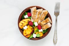 Salada do verão com galinha e pêssego grelhado, queijo de feta e framboesas em uma bacia com forquilha Alimento saudável fotos de stock royalty free Salada do verão com galinha e pêssego grelhado, queijo de feta e framboesas em uma bacia com forquilha Alimento saudável fotos de stock royalty free