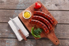 Salchicha asada a la parrilla en un tablero de madera con la salsa y las verduras Foto de archivo