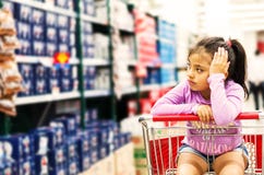 Sale, consumerism and people concept - happy little girl pensive in shopping cart royalty free stock image Sale, consumerism and people concept - happy little girl pensive in shopping cart royalty free stock image
