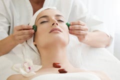 Salon de station thermale : Jeune belle femme ayant le massage facial avec Ston photos libres de droits Salon de station thermale : Jeune belle femme ayant le massage facial avec Ston photos libres de droits